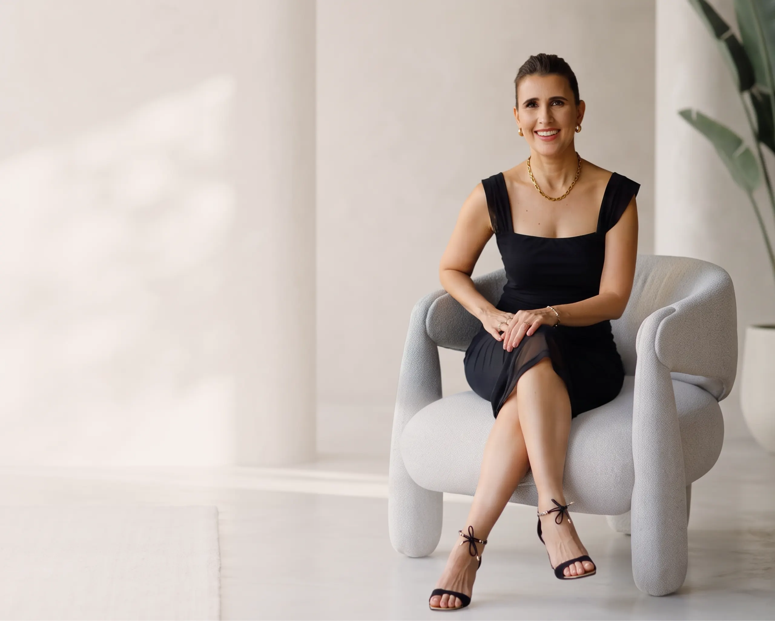 Dra. Carolina Lins, dermatologista, sentada em uma poltrona clara no consultório
